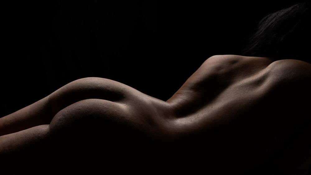 Artistic nude photography emphasizing curved forms with dramatic side lighting.