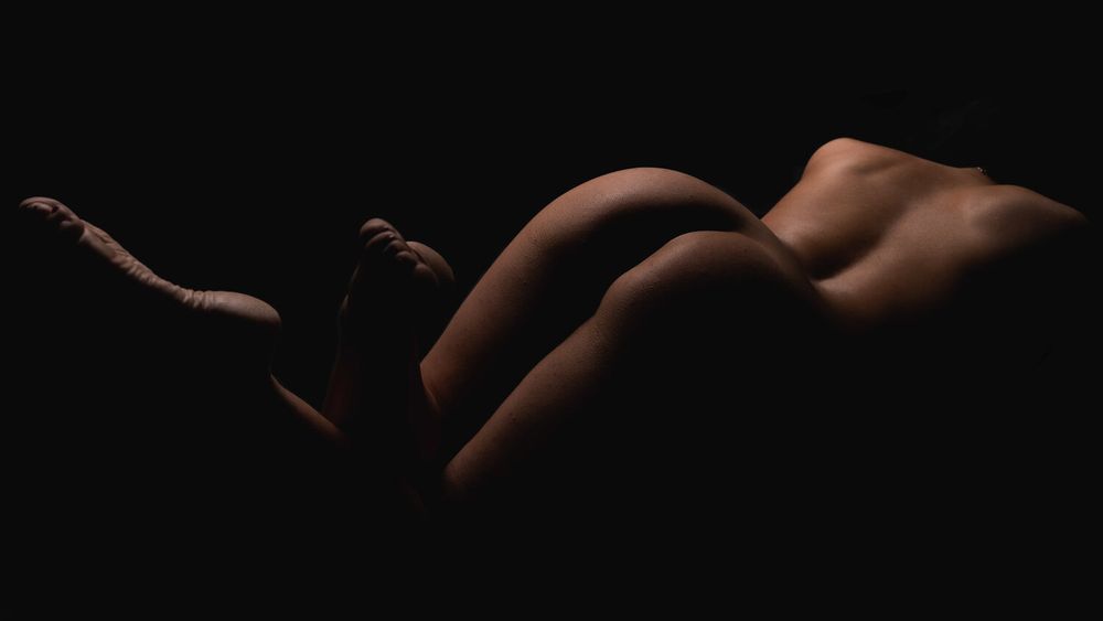 Abstract bodyscape photography highlighting natural curves in warm tones against black.