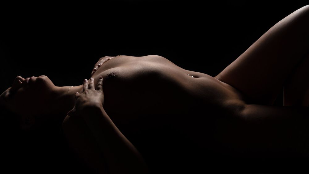 Artistic nude photograph emphasizing natural curves and shadows in warm lighting.