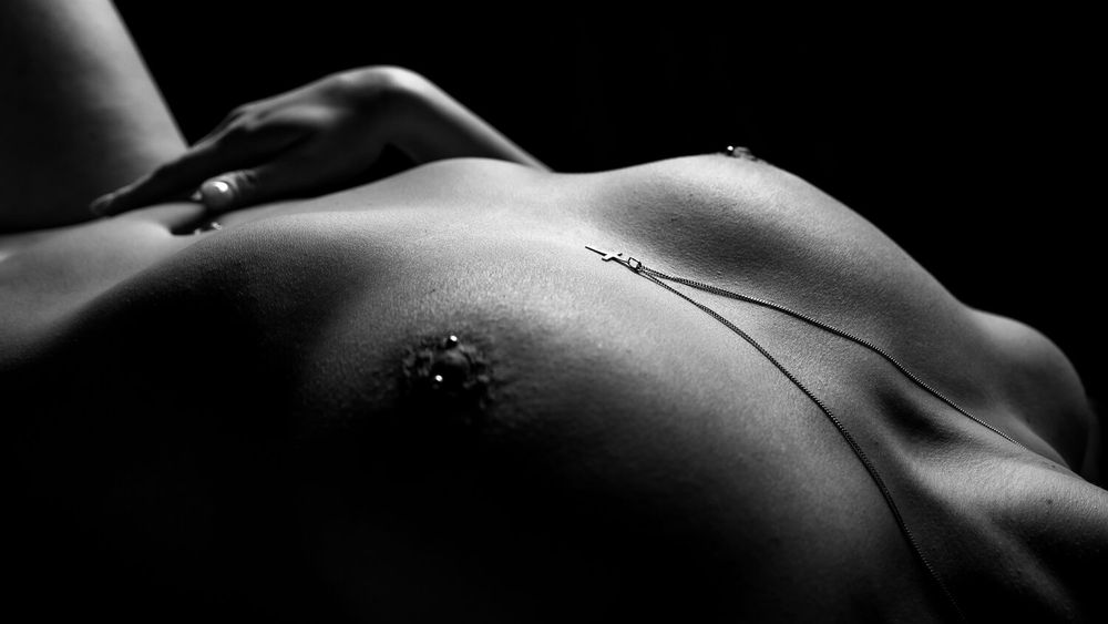 Artistic black and white close-up of a torso with body jewelry in dramatic lighting.