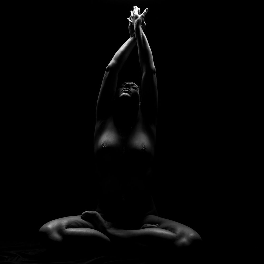 Artistic nude silhouette with raised arms creating graceful lines against black background.