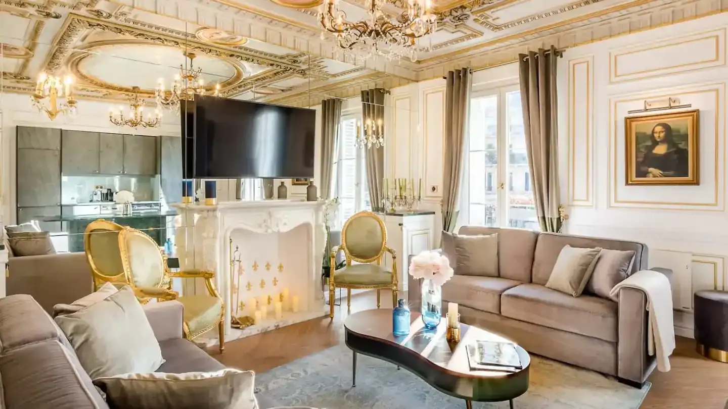 Opulent living room features ornate moldings, chandelier, and modern furnishings in a Parisian apartment.