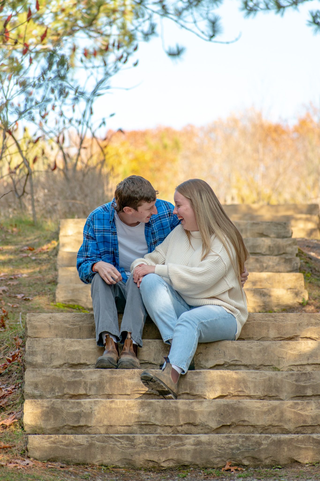 A romantic couple sits on stone steps in a park during autumn season.