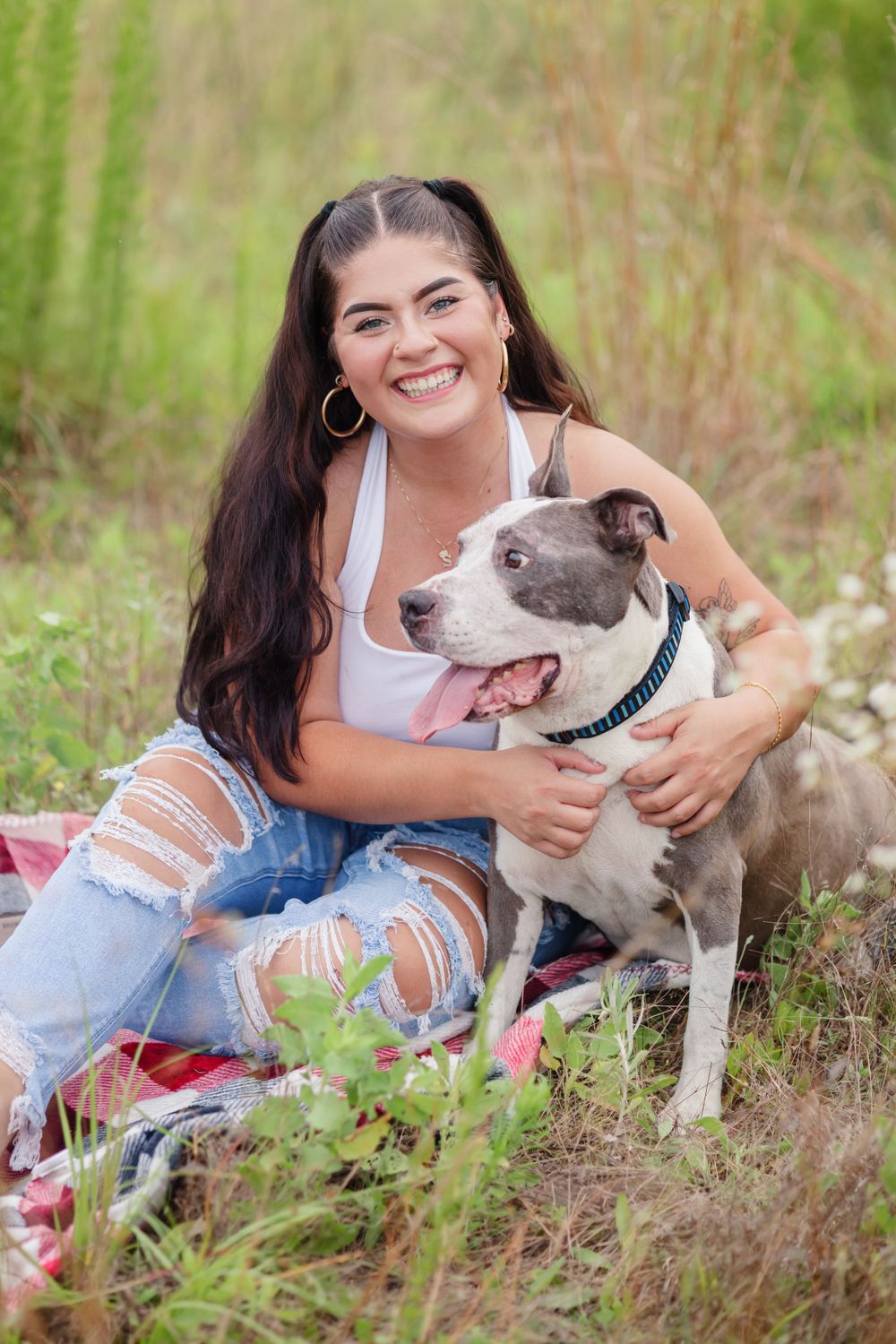 Woman with dark hair hugging her grey and white pit bull dog in a summer field.