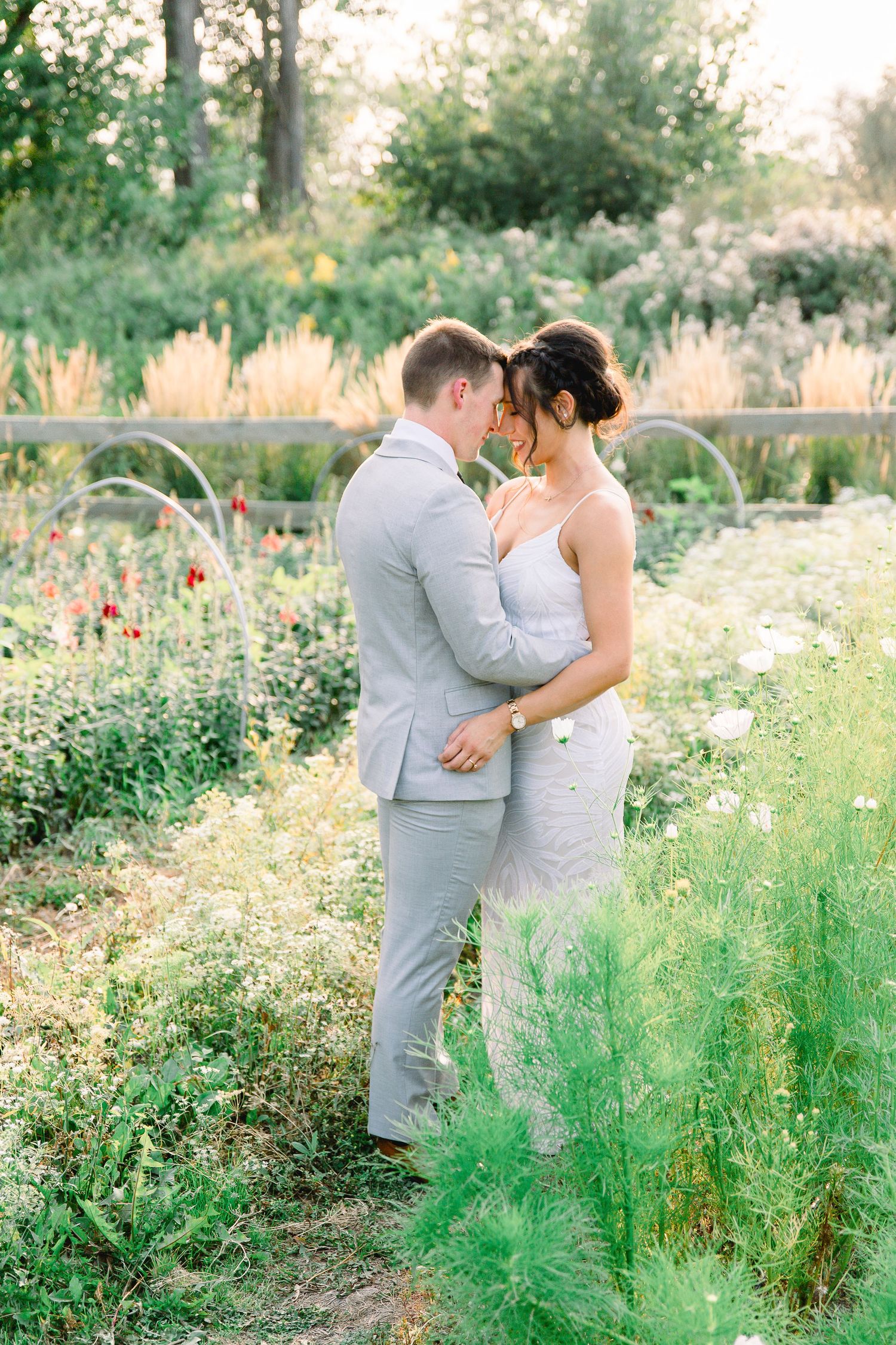 Newlyweds embrace in garden setting with light grey suit and white dress.