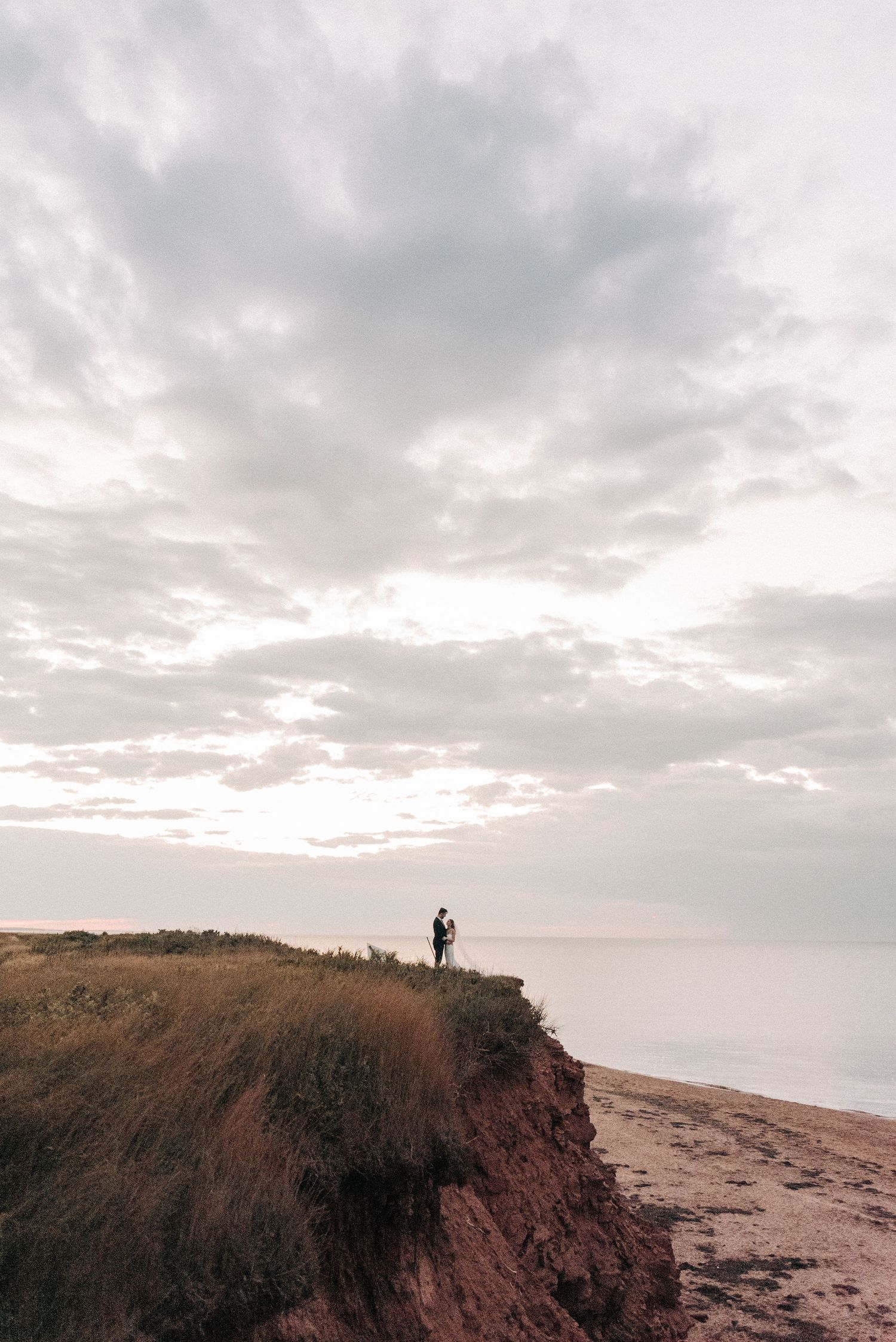 A silhouetted figure stands alone on a coastal cliff edge against a cloudy sky.