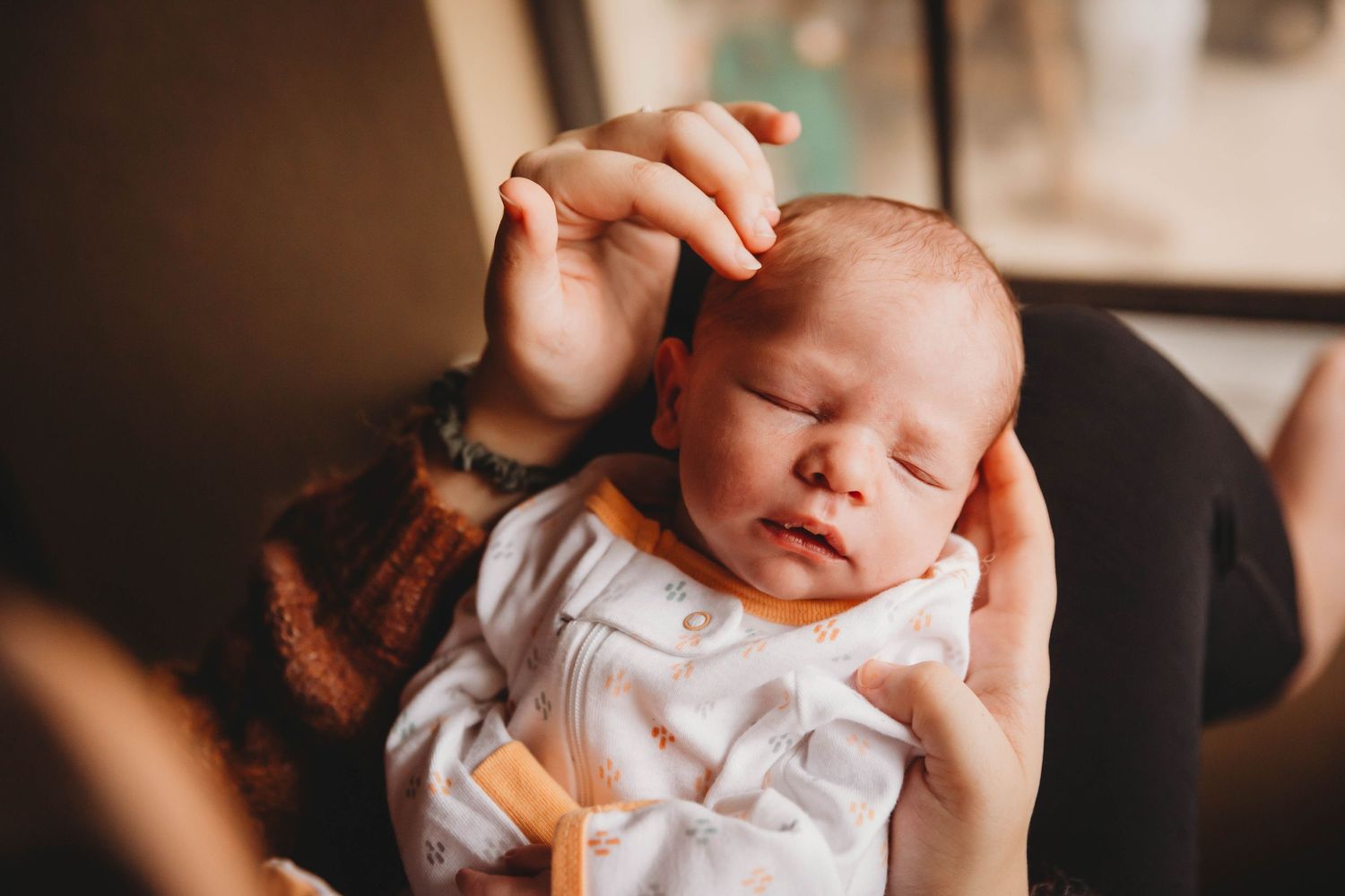 Close-up shot of sleeping newborn baby in white onesie being gently cradled.