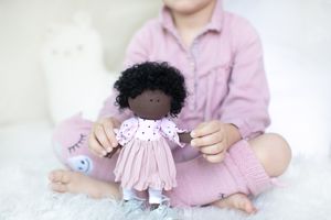 Young child holding a small handmade dark-skinned fabric doll in a pink dress.