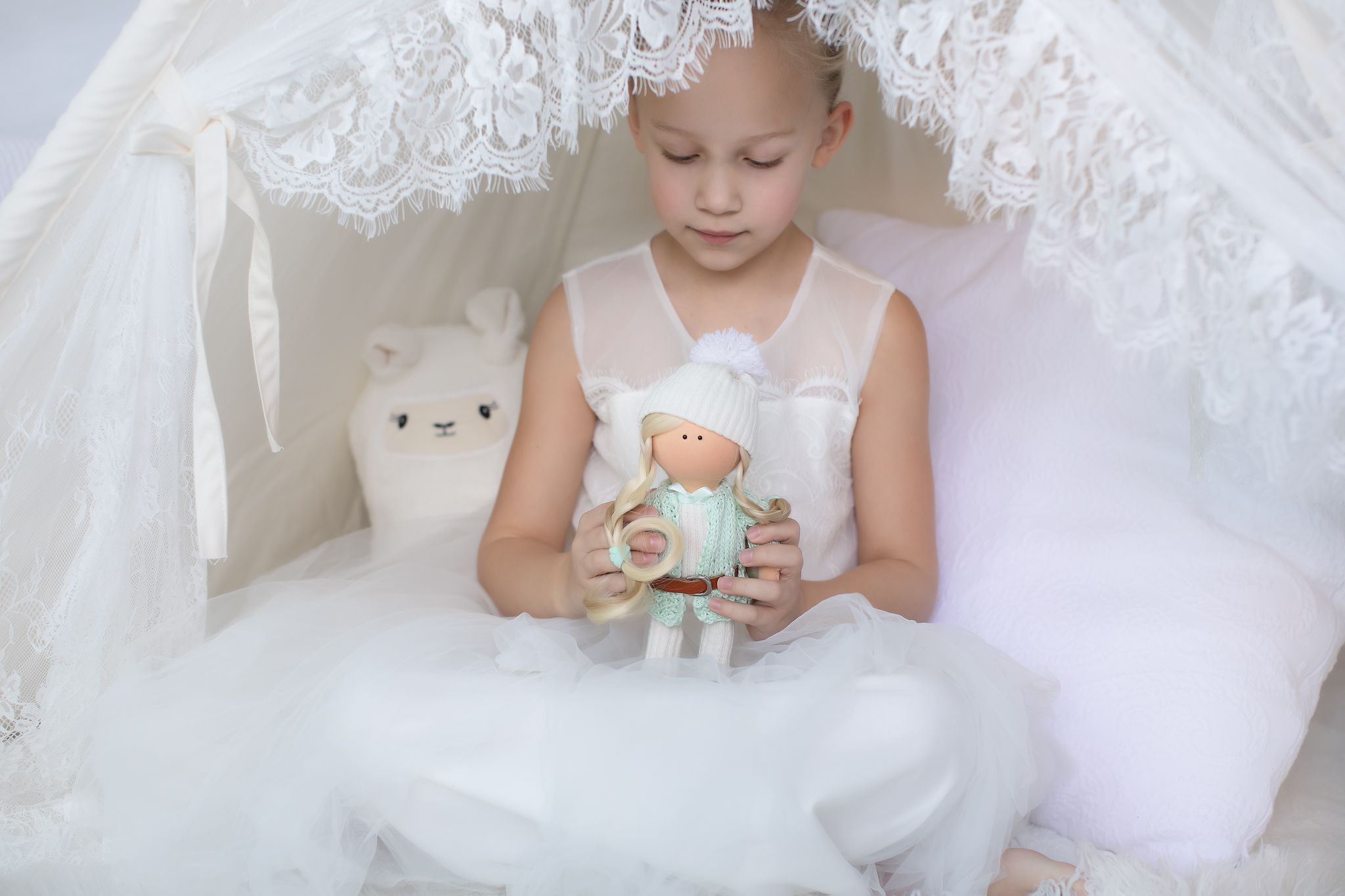 Young girl in white tutu dress holding a small handmade mint doll inside a white lace teepee.