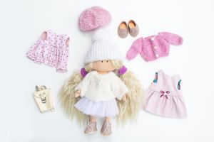 Handmade blonde fabric doll displayed with pink accessories including dresses, cardigan, and shoes.