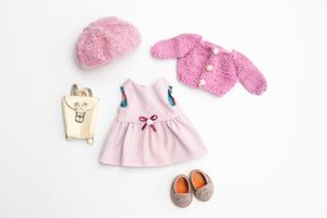 Flat lay of handmade doll accessories including a pink dress, knit cardigan, beret, and gray shoes.