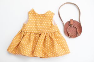 Yellow polka dot sleeveless doll dress with a brown round tassel crossbody bag on white background.