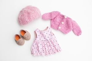 Flat lay of handmade doll clothing set with pink polka dot dress, knit cardigan, beret, and shoes.
