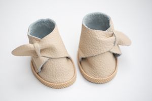Pair of beige leather baby shoes with bow detail and blue lining on white background.