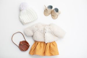 Doll outfit flat lay with white fur coat, yellow polka dot skirt, knit hat, bag, and shoes.
