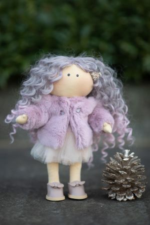 Handmade doll with curly lavender hair wears a pink faux fur coat and tulle skirt beside a pine cone.