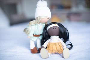 Two handmade cloth dolls, one blonde in mint knit wear and one dark-haired in gold skirt, posed together indoors.