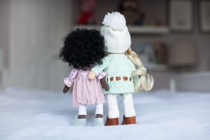 Two handmade dolls seen from behind, one with curly black hair in pink and one blonde in mint green outfit.
