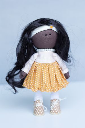 Handmade fabric doll with long black hair wearing a yellow polka dot skirt and white sweater.