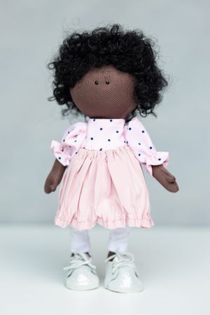 Handmade dark-skinned fabric doll with curly black hair in a pink polka dot dress and white sneakers.