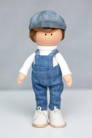 Handmade boy fabric doll wearing denim overalls, white turtleneck, and a gray flat cap.
