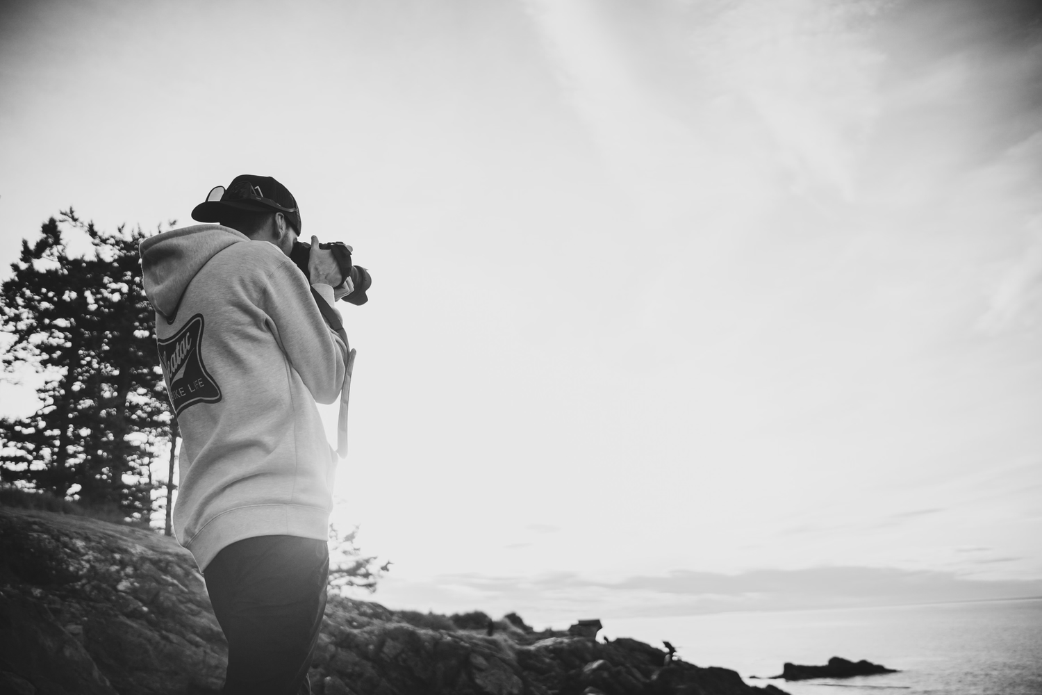 Silhouette of person photographing scenic coastal landscape in black and white.