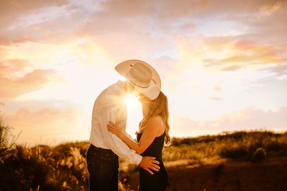 engaged cowboy couple kissing with the sunset beaming behind them
