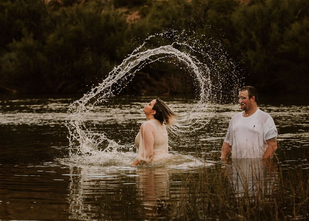maternity couple in a lake while she flips her hair in the water