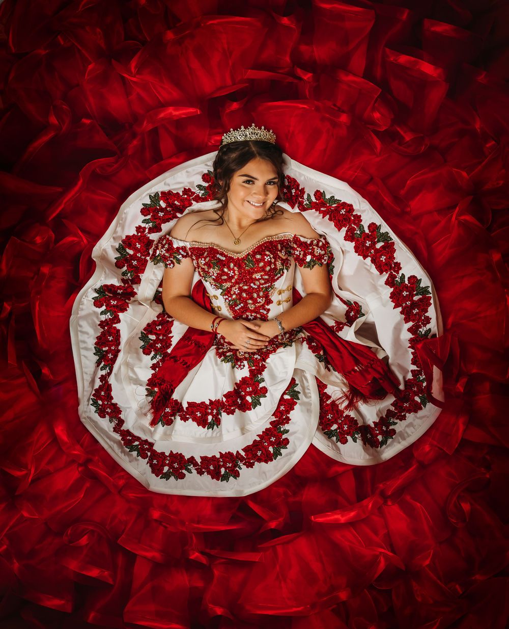 girl laying down wearing crown and red fiesta quinceanera dress with fllowers