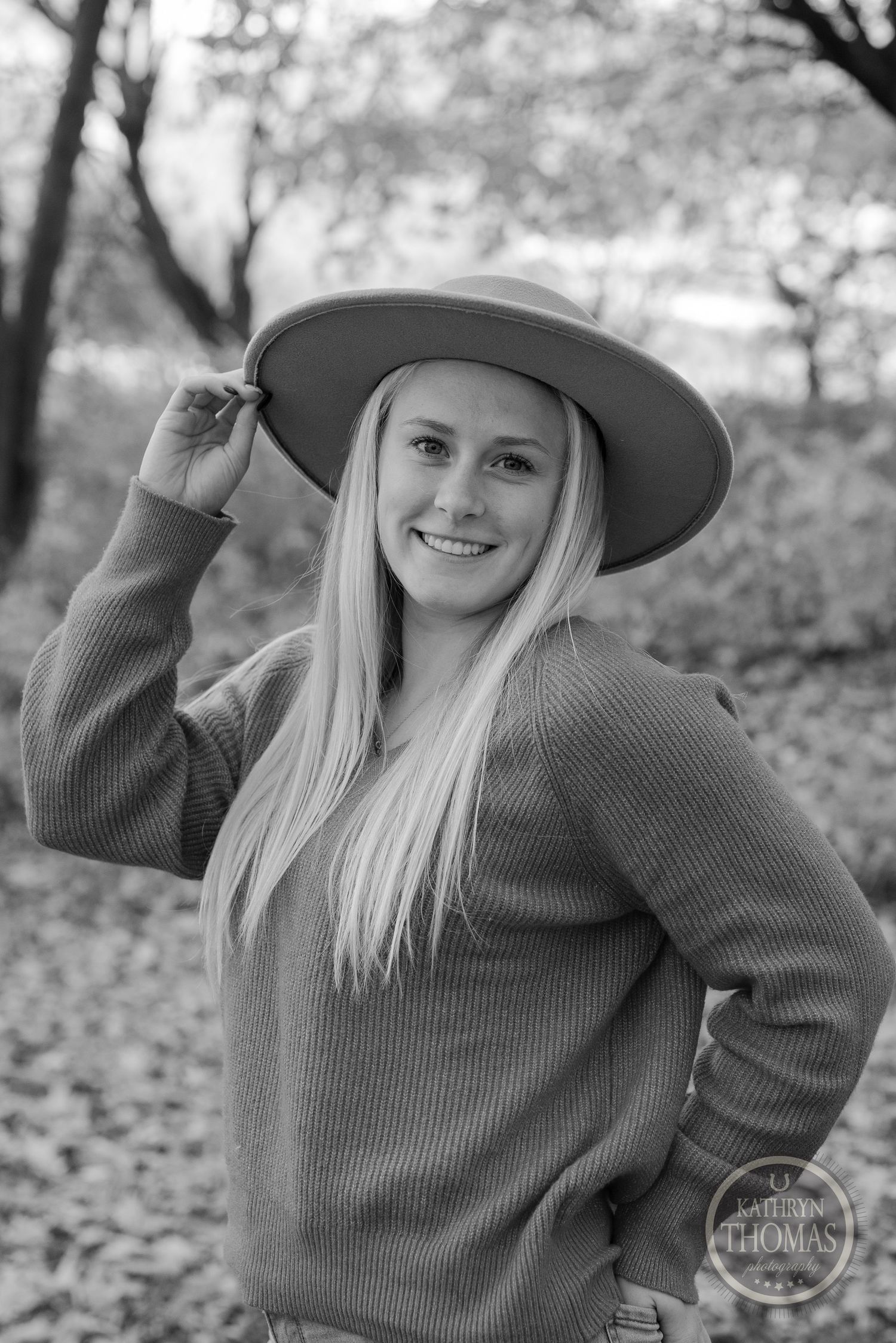 Black and white portrait wearing wide brim hat and sweater in autumn setting.