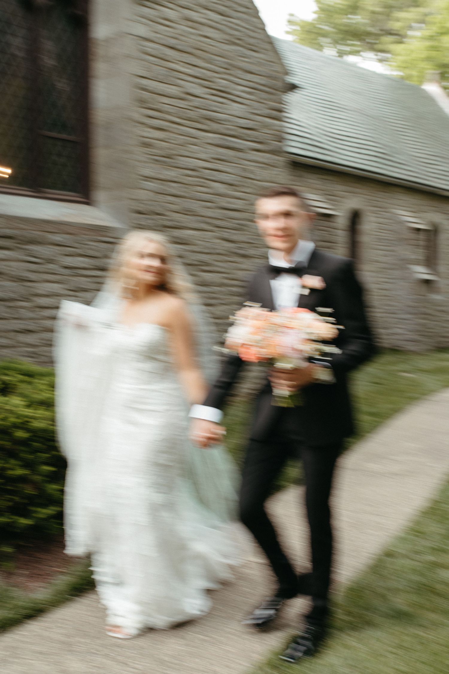 A blurred wedding photo showing a couple walking together outside a stone building.