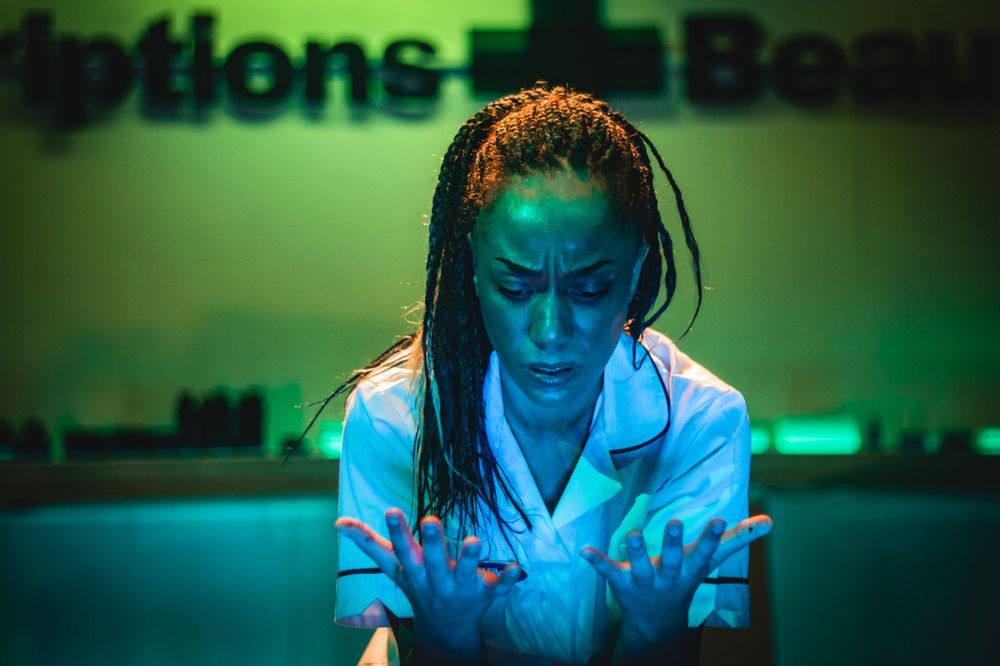 A performer in white attire illuminated by green stage lighting during a dramatic moment.