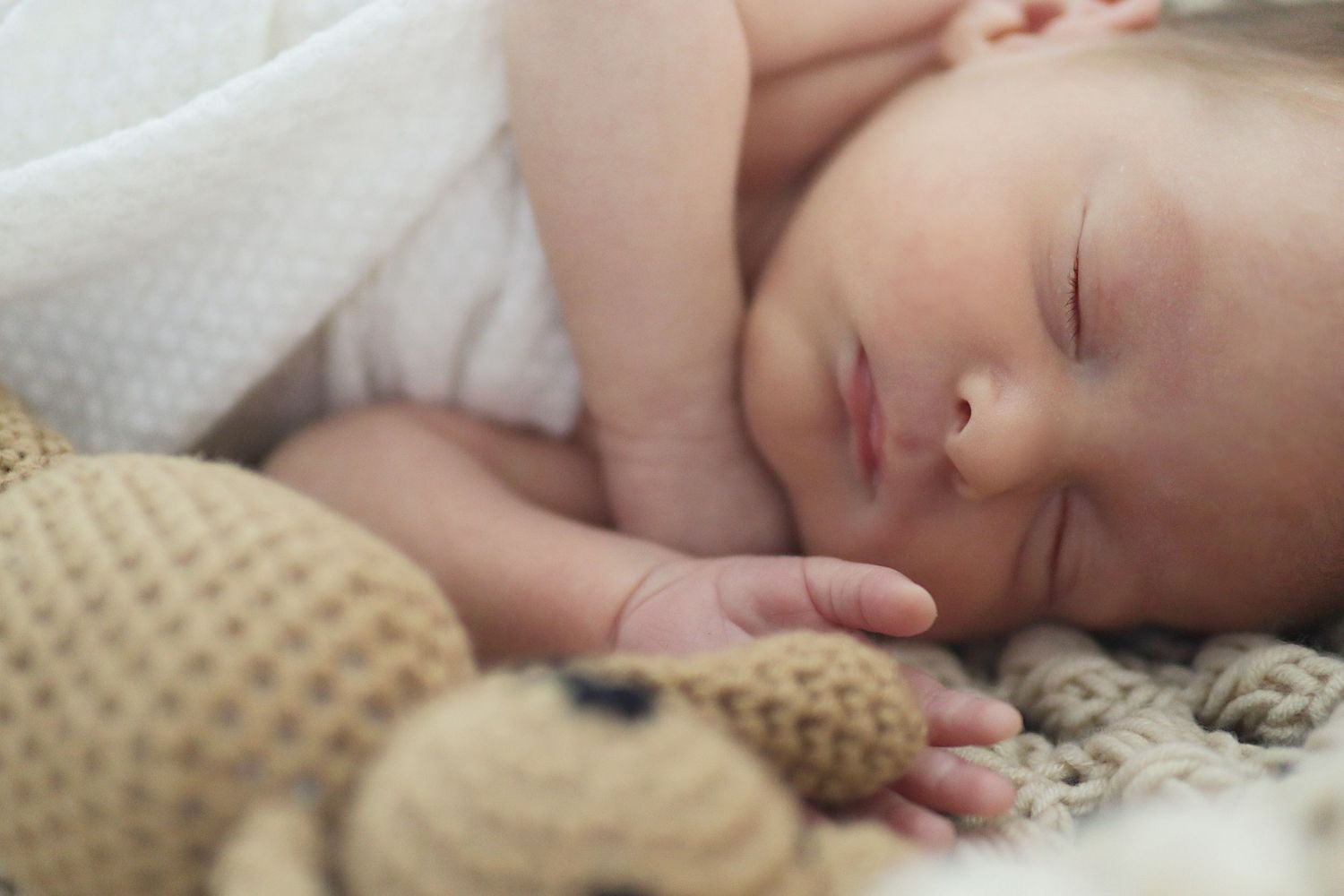 Peacefully sleeping baby with a brown knit teddy in the foreground