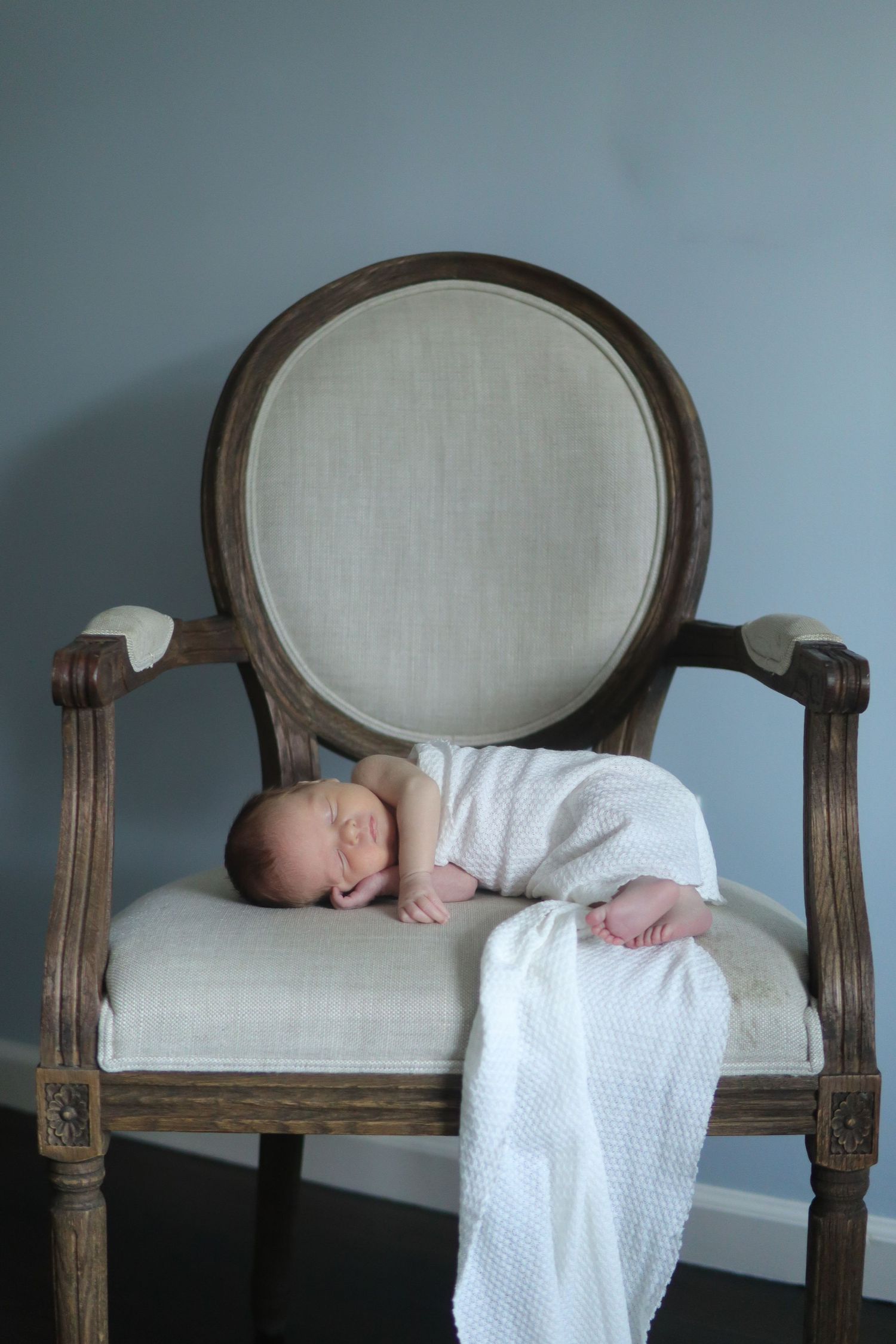 Newborn sleeping on a vintage arm chair wrapped in a soft white blanket
