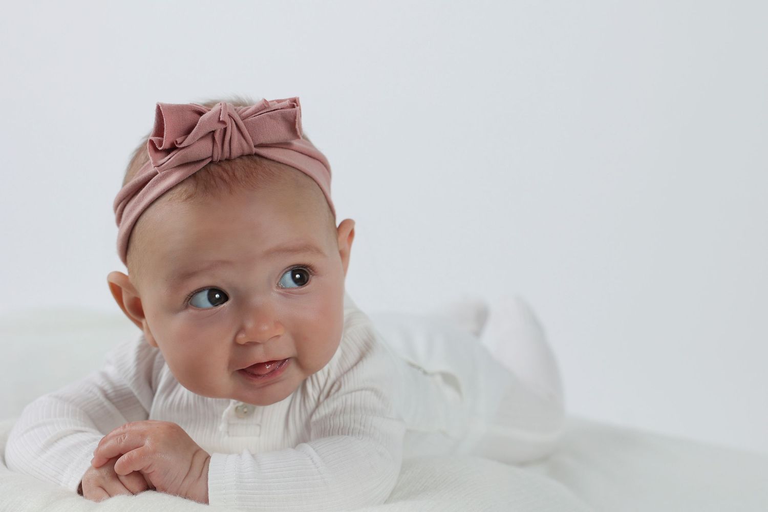 infant girl with a pink headband playing on her stomach
