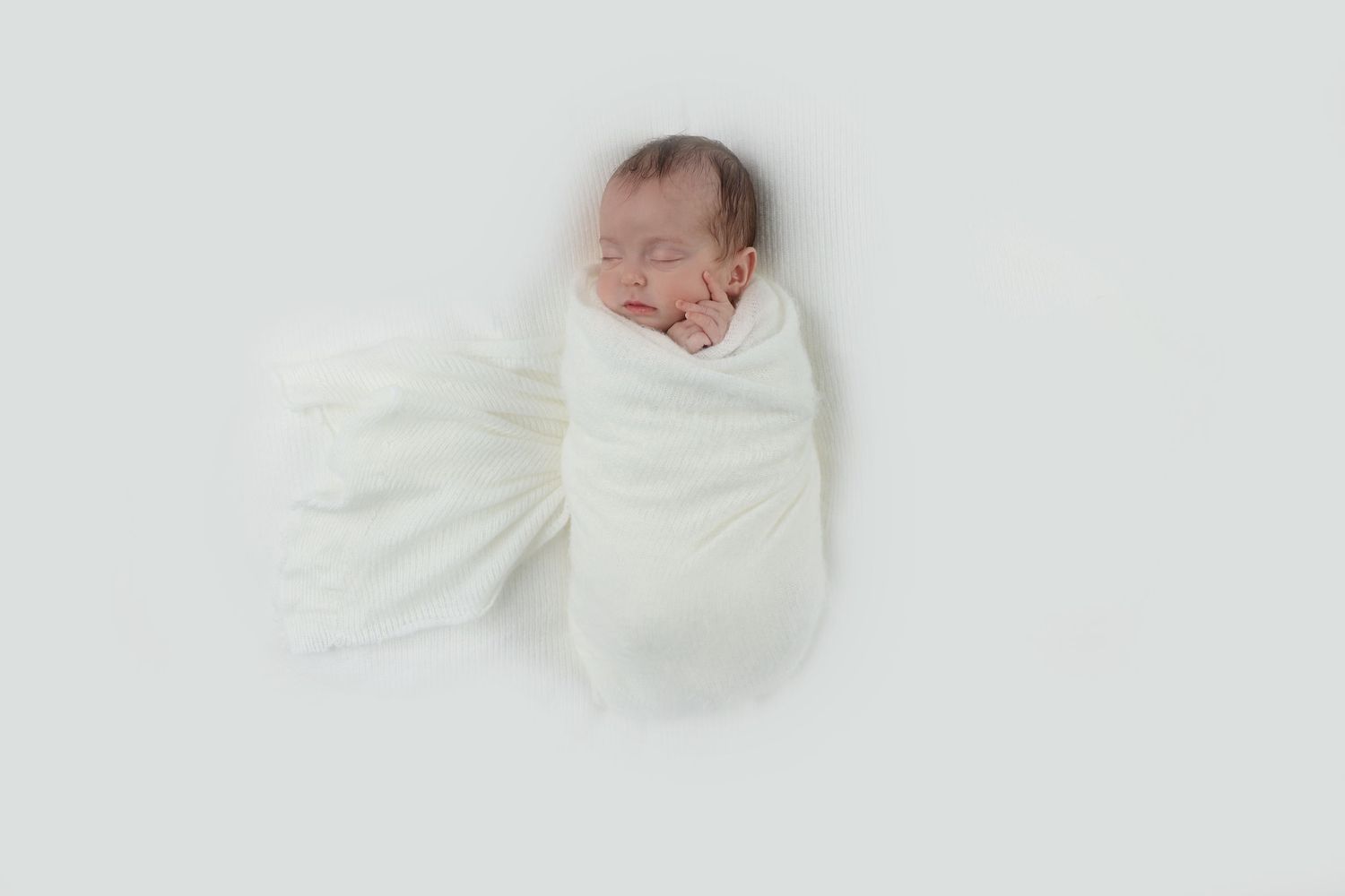 Sleeping newborn wrapped in a soft white swaddle with her fingers peeking out
