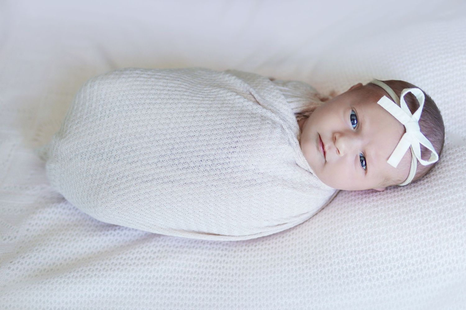 awake newborn girl wrapped in a pink swaddle with a white boy