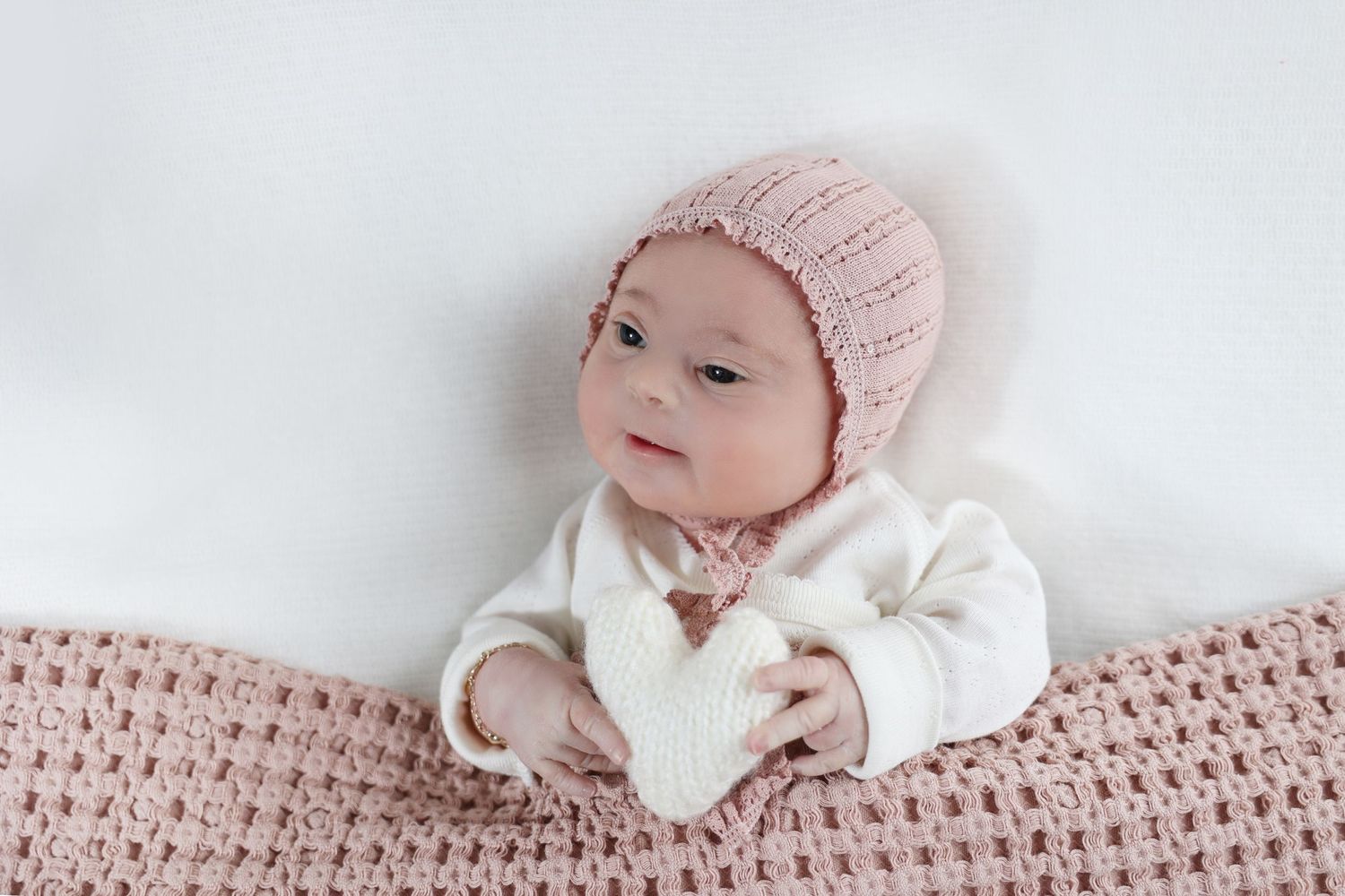 wide eyed Newborn holding plush knit heart
