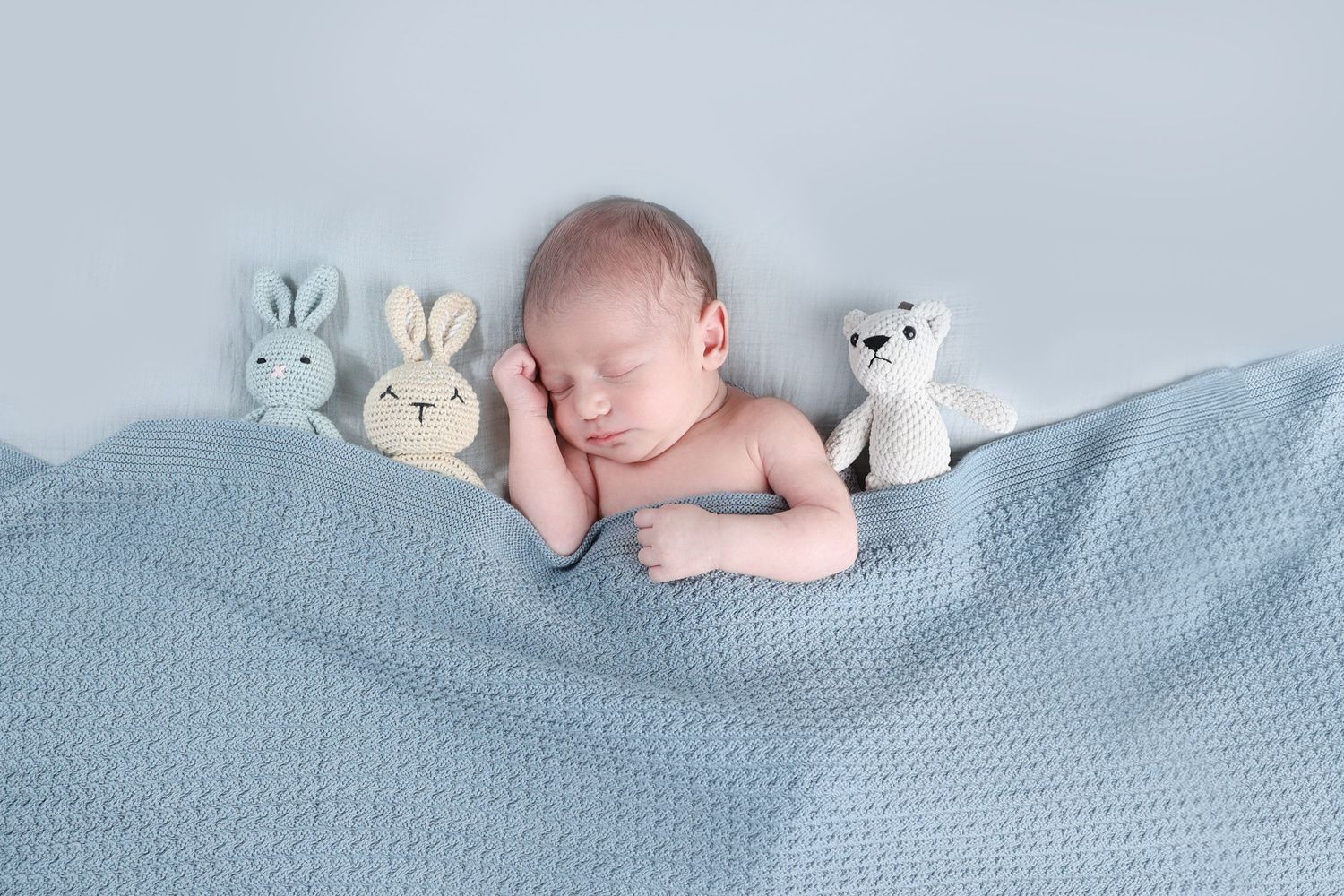 sleeping newborn surrounded by plush knit teddy bears