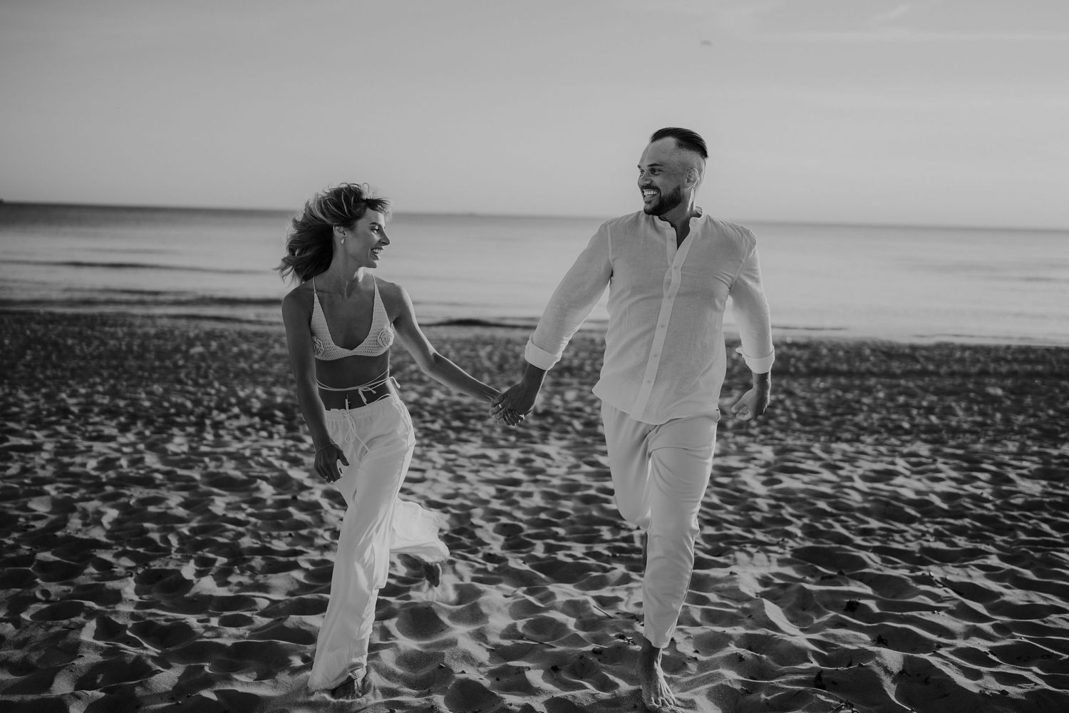 A couple walking and laughing together on a beach in black and white.