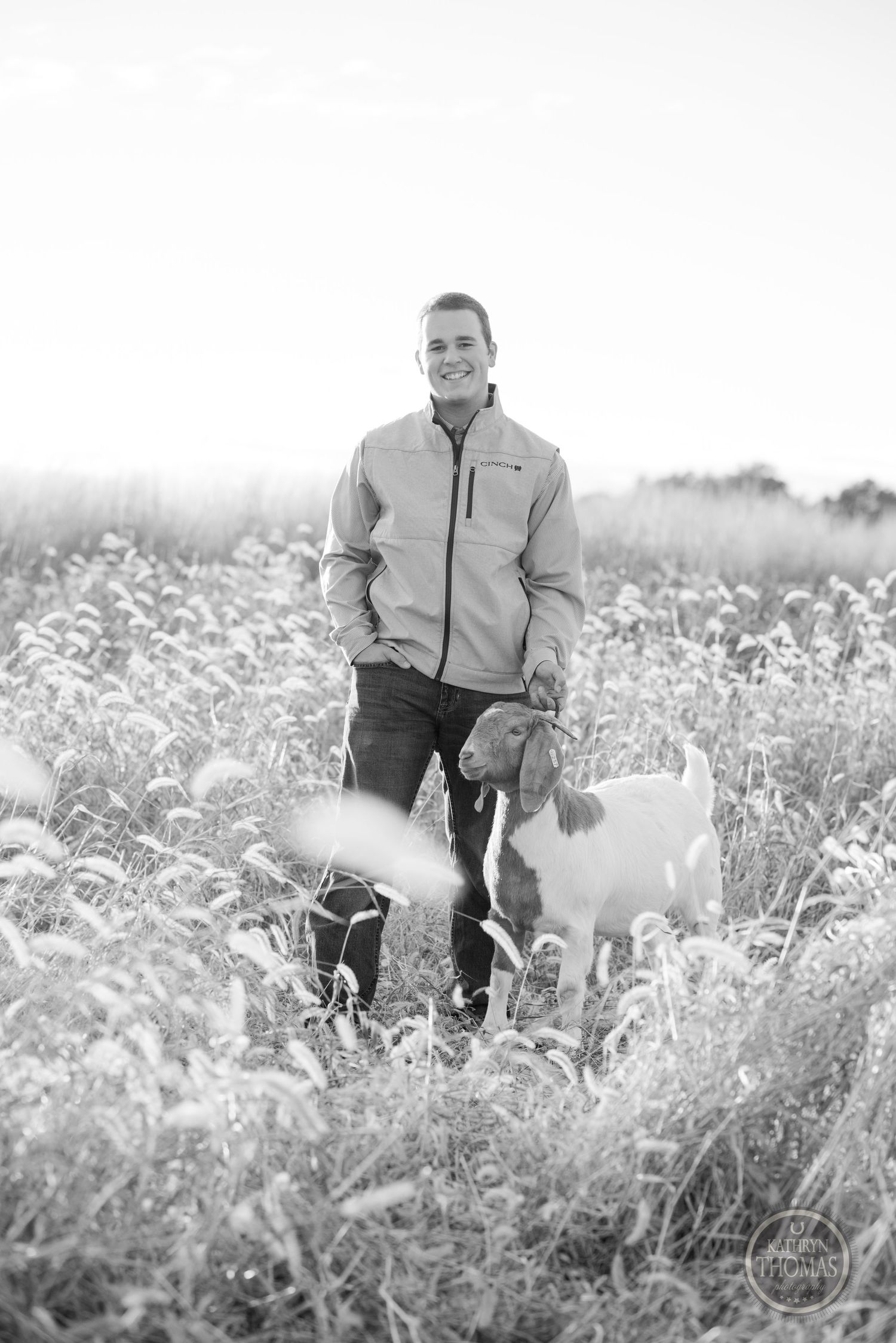 Black and white portrait of person with goats in field of tall grass.