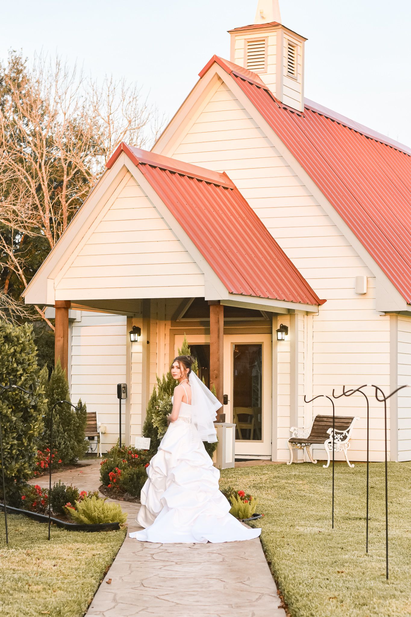 White chapel with red roof and bridal portrait on pathway.