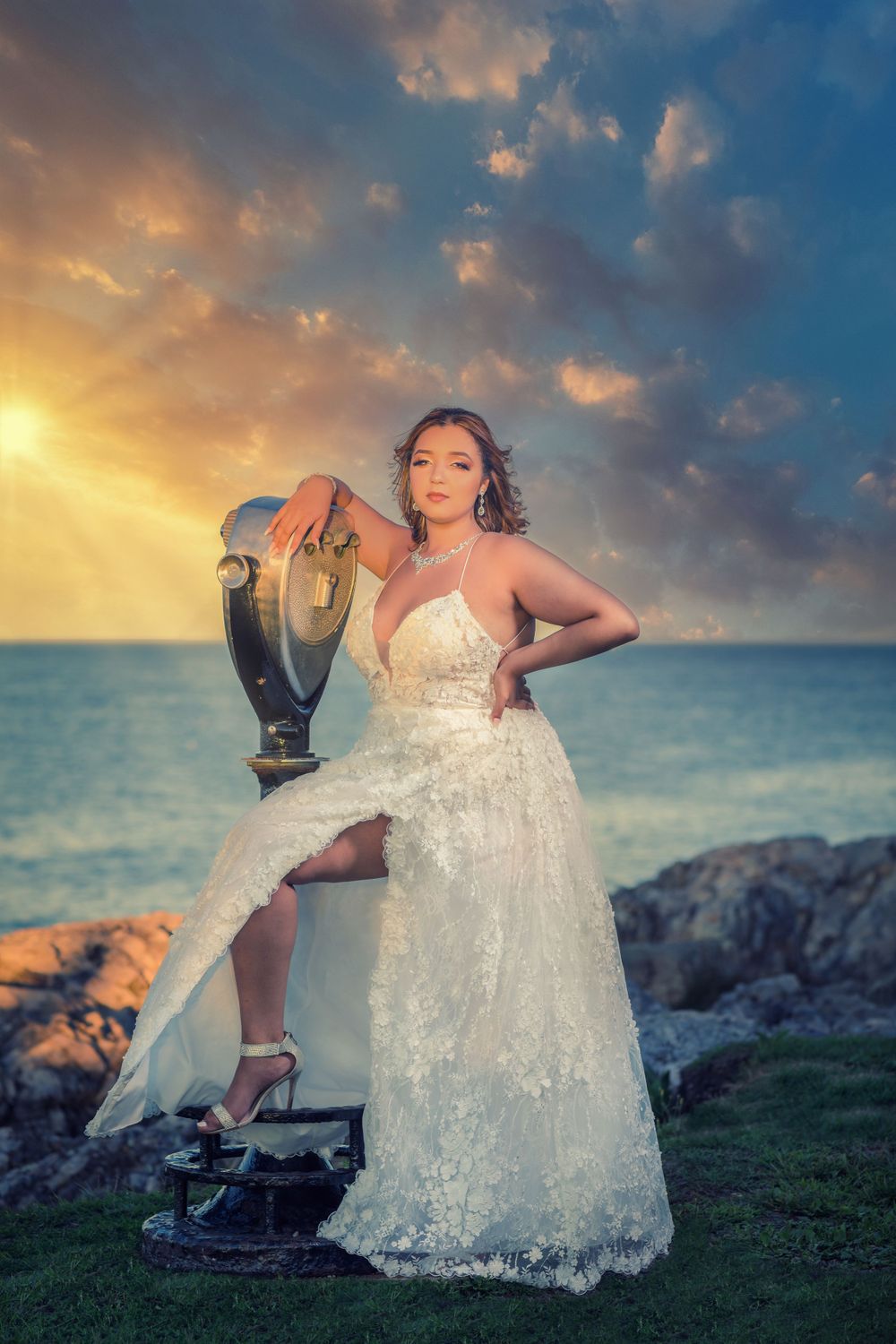 A sparkling white lace dress flows elegantly against a dramatic sunset sky by the ocean.