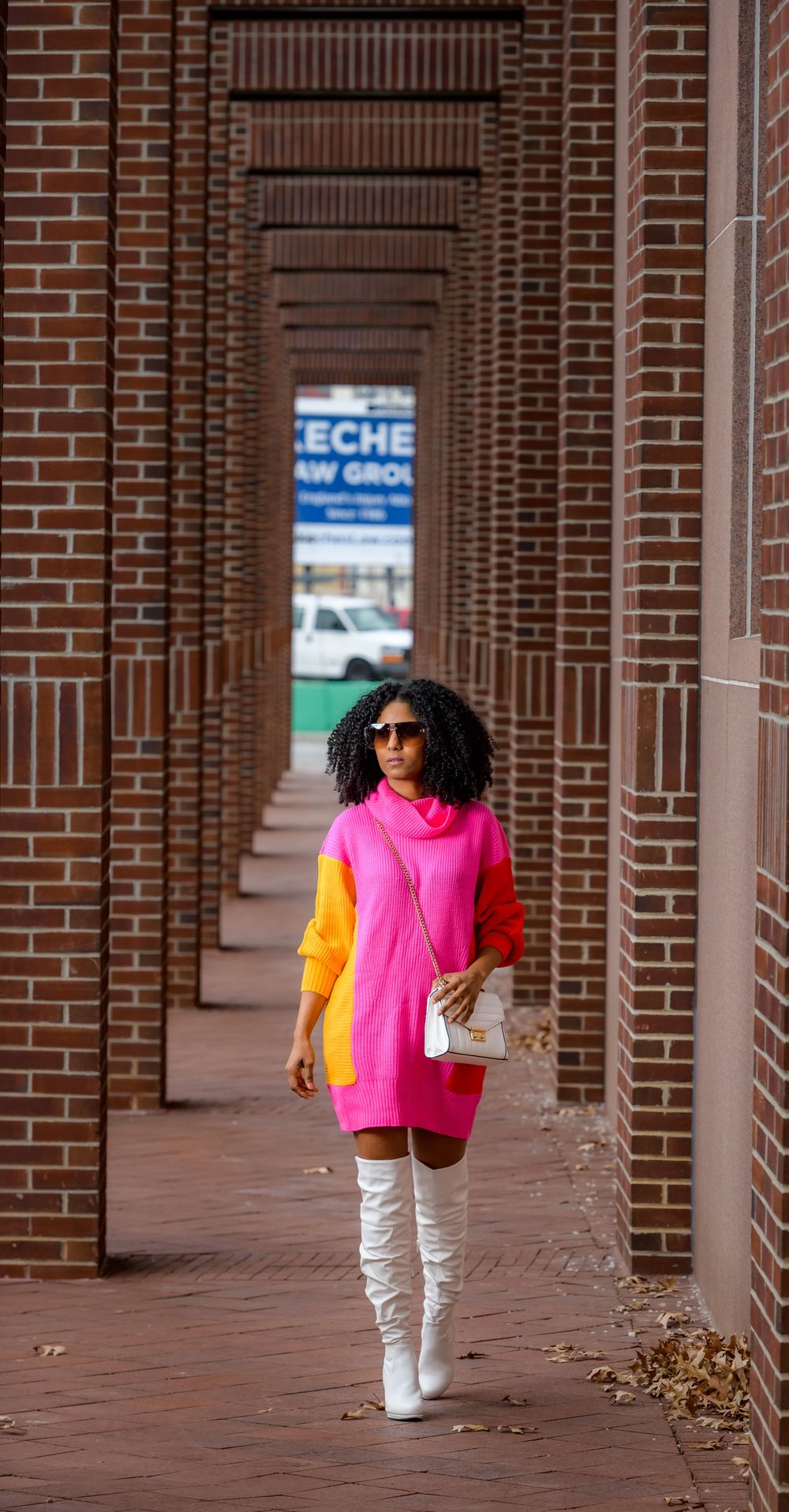 A colorful outfit featuring pink and orange tops with white pants stands in a brick columned walkway.