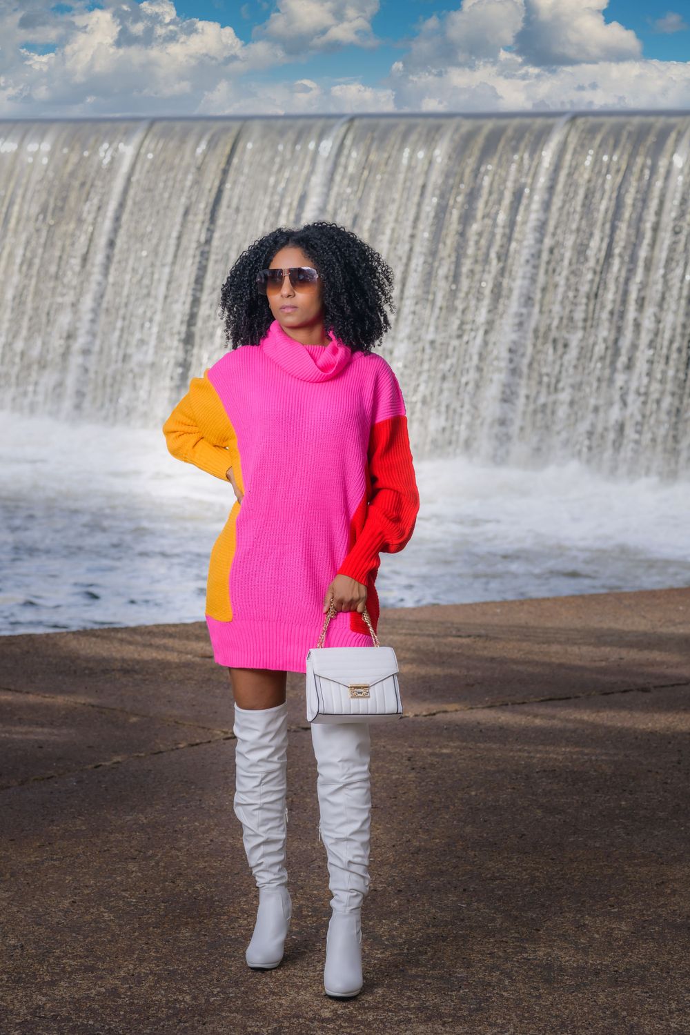 A bright color-block outfit stands near a cascading waterfall on a sunny day.
