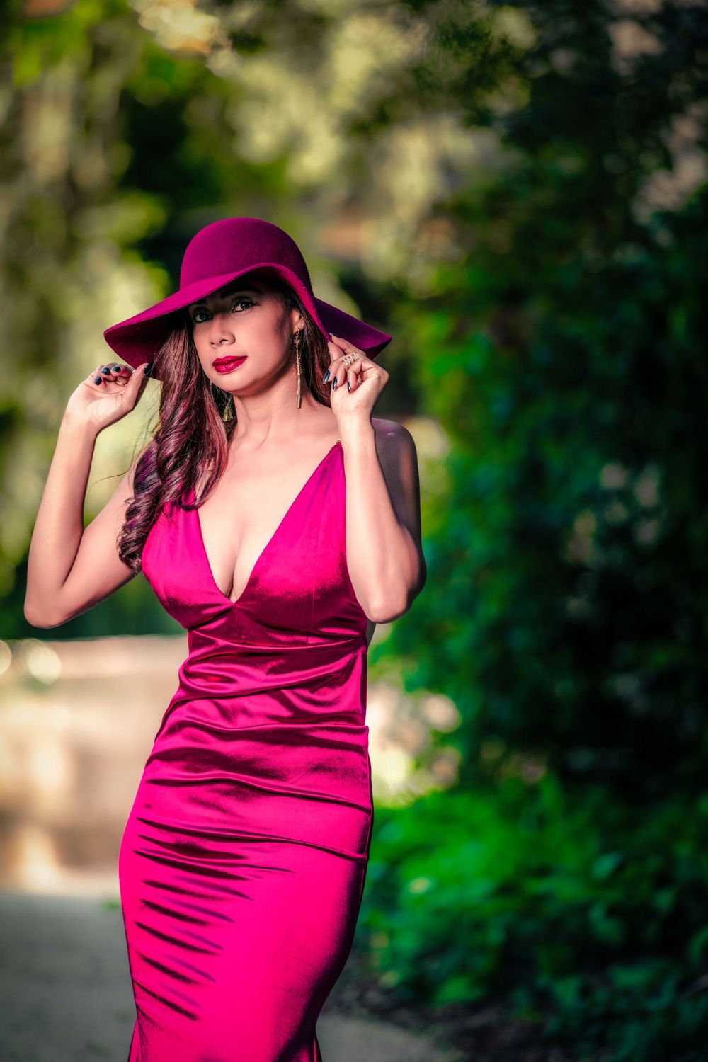A deep magenta satin dress photographed in a lush garden setting.