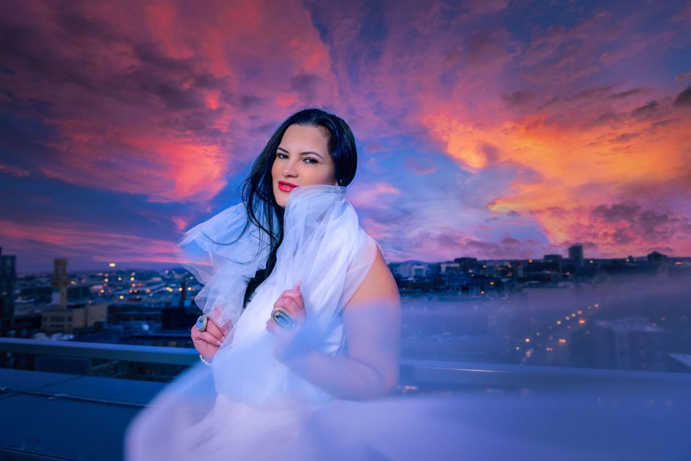 A flowing white dress catches the light during a dramatic purple and pink sunset.