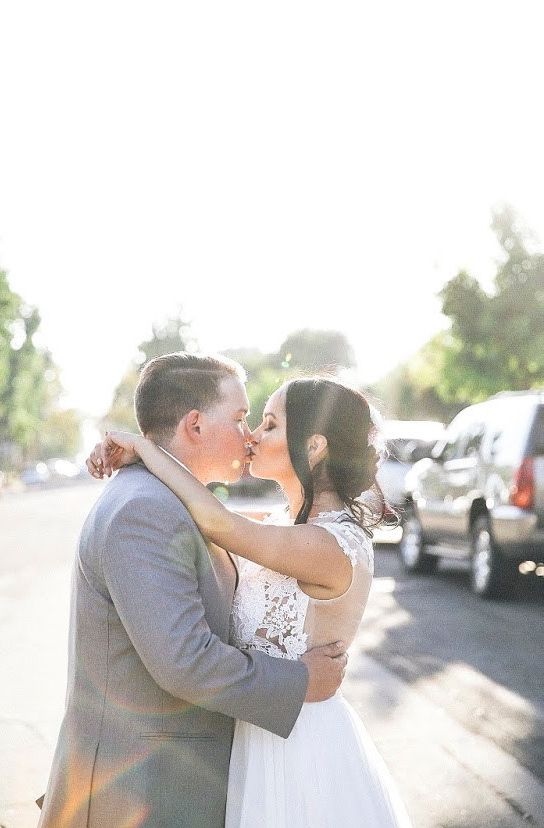 A couple shares a romantic moment together during a sunlit wedding photo session in a parking lot.