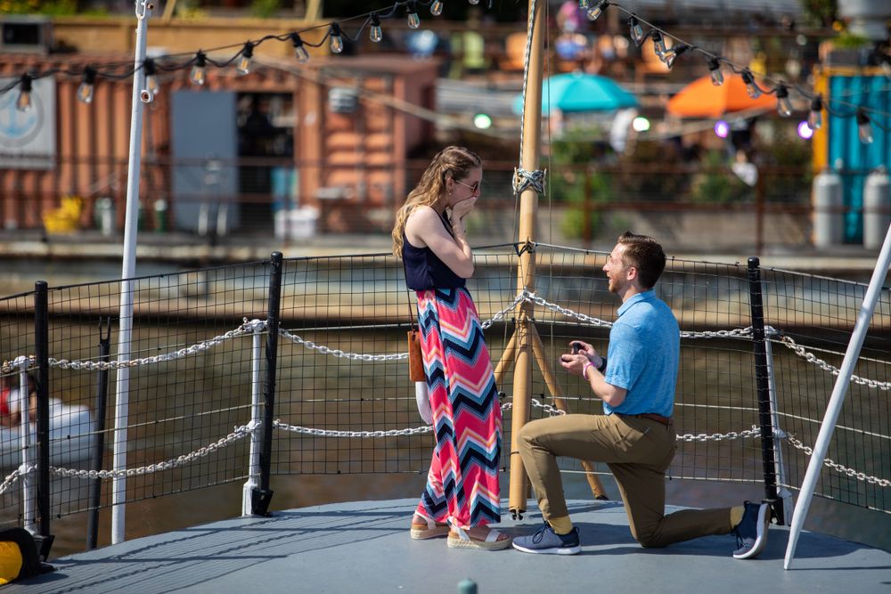 Romantic proposal moment captured on waterfront deck at sunset.