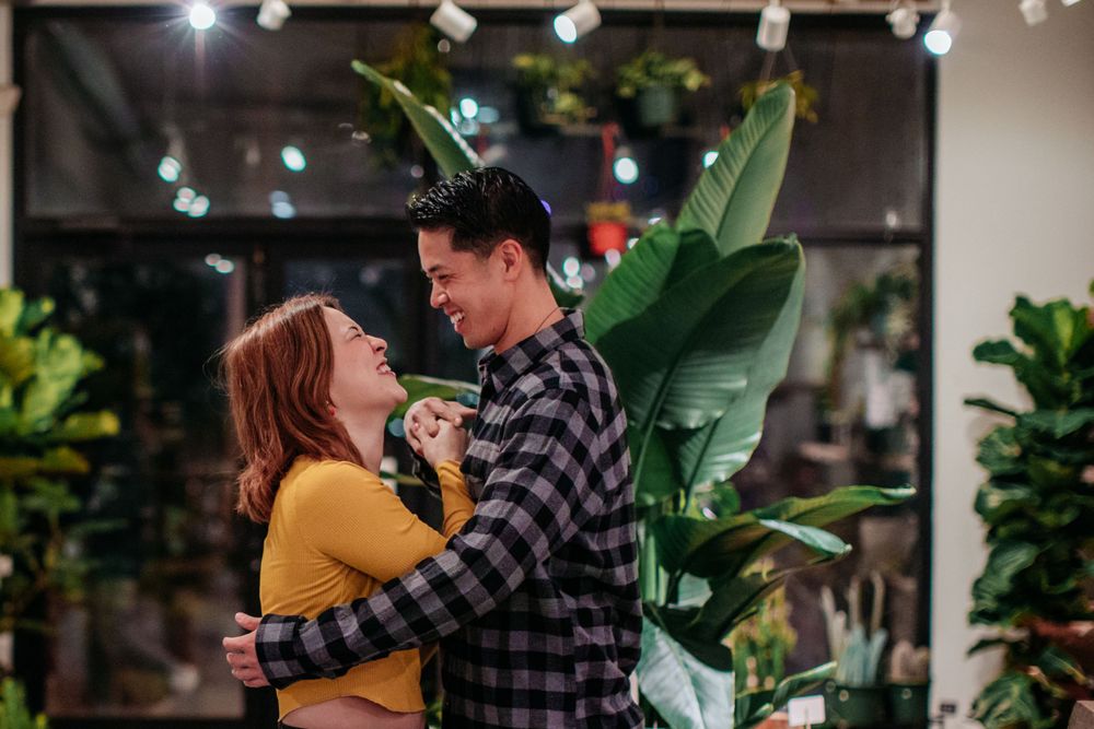 A couple embracing in front of large tropical plants in an indoor garden setting.